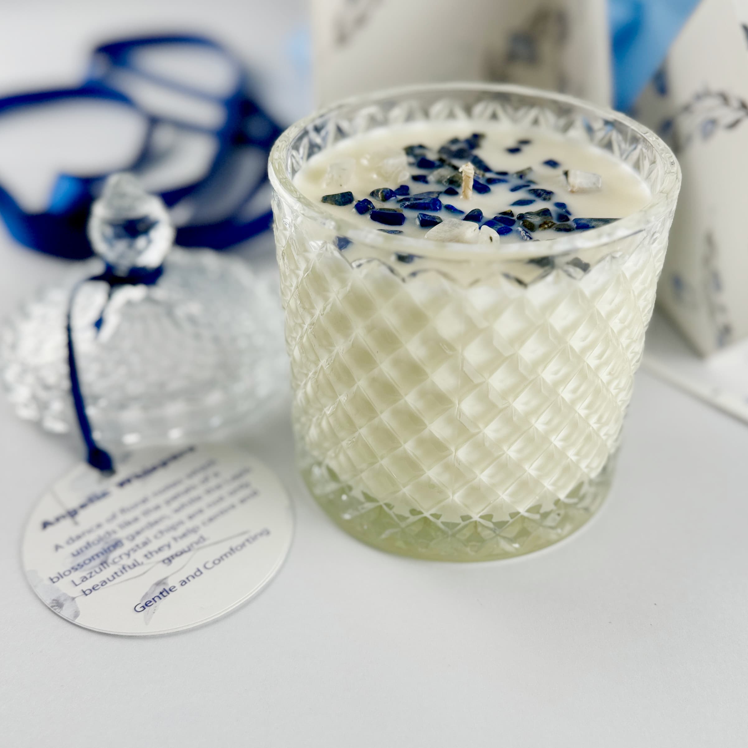 Close up of floral handpoured soy wax candle in Art Deco Crystal Glass embellished with lapus lazuli. The lid is off and beside it with a label tied in navy blue ribbons sitting beside the candle