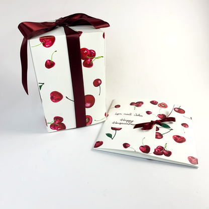 Cherry love candle box featuring scattered cherries and tied with burgundy ribbon. to The right, a card folder featuring scattered cherries and smaller burgundy bow, and the words, Happy Housewarming
