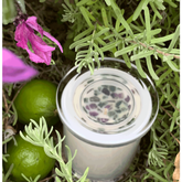 top down view of lavender and lime scented soy candle nestled in lavender bush with lavender flowers- amethyst and green aventurine crystals embellish the candle and two limes site beside