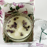 magnolia scented rose quartz and amethyst embellished hand poured soy wax candle in pink magnolia blossom printed product box. Lid is off the candle to the right and partial view of the product label at the bottom right can be seen
