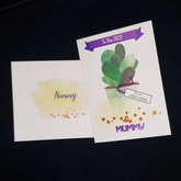This is two images, one of the envelope and another of the front of the card. The front of the envelope has a splotch of yellow in the centre with gold dots below it. It has the word Mummy written on it. The front of the card has the words "To The Best" written in white on the purple banner. On the tag attached to the pot is written " You are AMAZING&