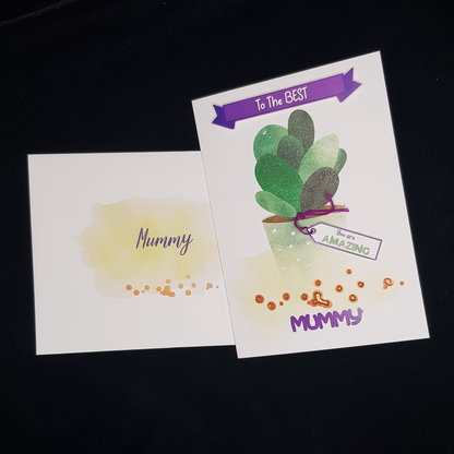 This is two images, one of the envelope and another of the front of the card. The front of the envelope has a splotch of yellow in the centre with gold dots below it. It has the word Mummy written on it. The front of the card has the words &quot;To The Best&quot; written in white on the purple banner. On the tag attached to the pot is written &quot; You are AMAZING&