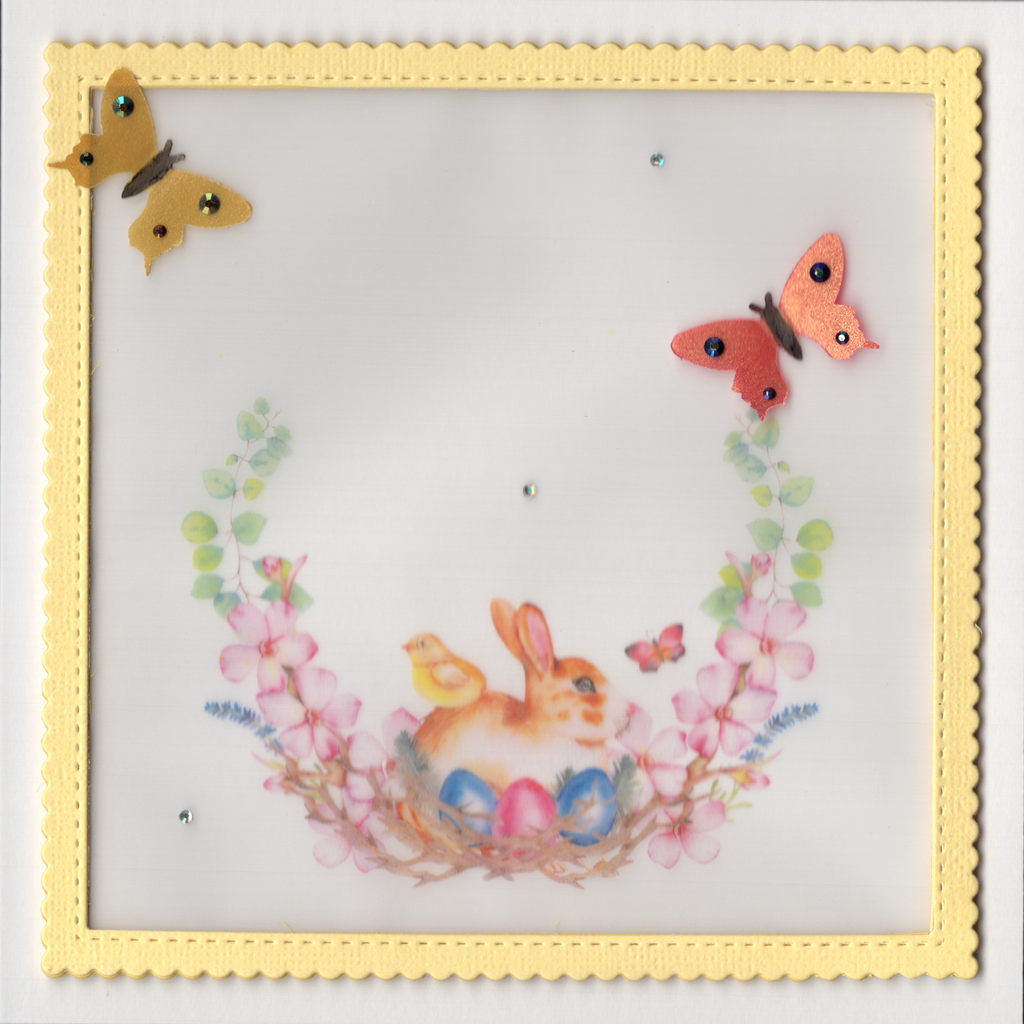 This beautiful card is printed on heavy Eggshell textured card stock. It features a raised framed panel of vellum which is secured in a yellow scalloped frame.  A cute bunny with a chick on its back sits behind Easter Eggs nestled in a wreath of flowers. Two butterflies with jewels on their wings sit proudly. Glossy accents on the eyes of the bunny and chick and in the centre of the flowers provide the finishing touches to this delicate card.