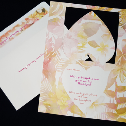The entire inside of the card background consists of paler tropical flowers and foliage. A white heart slightly smaller that the cutout heart sits centrally overlaid on tropical flowers. A thank you message is written in an apricot colour with the verse in the same pink as the front. Fully customisable
