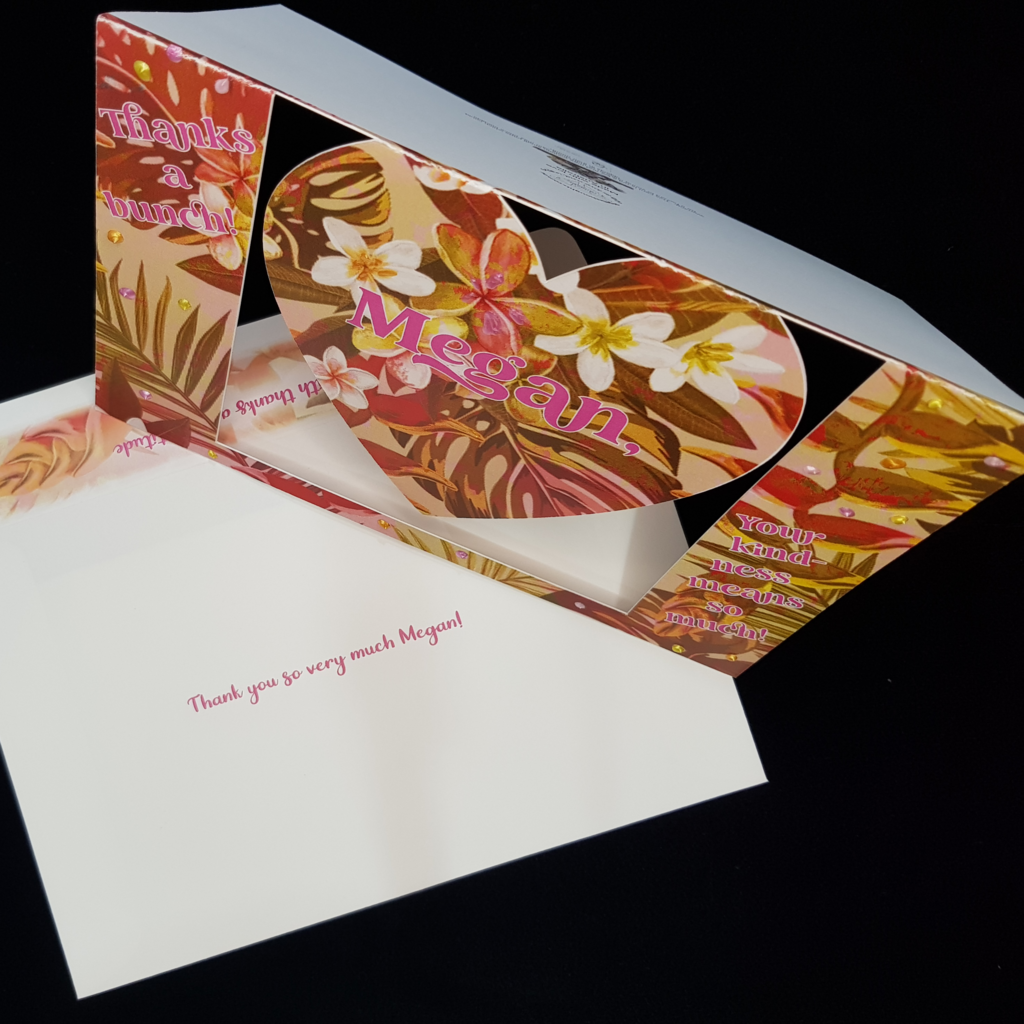 A beautiful heart swing card stands up on a matching envelope. with the words &quot;thanks a bunch&quot; on the left, the name Megan sits centrally on the swinging heart and another sentiment &quot;your kind-ness means so much&quot; sits on the right.  Tropical flowers and foliage are the focus of this muted green and pink toned background. Pops of pearl colours including yellow, orange and pinks have been selectively hand applied.