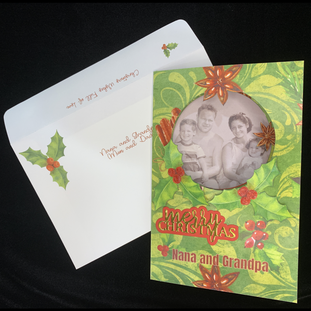 This is an image of the envelope and the card front with photo and text added. The envelope has a sprig of holly in top lefft corner on front and a small sprig of holly on the back flap. The card has a family photo added and Merry Christmas Nana and Grandpa