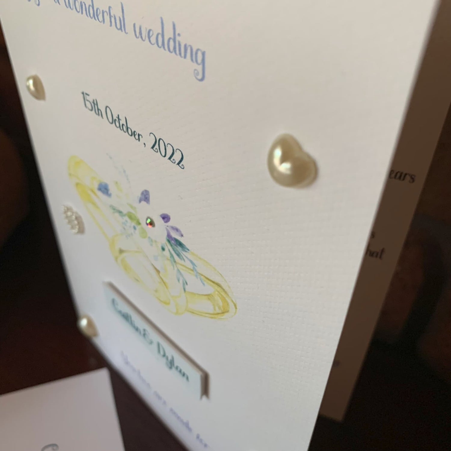 closeup of personalised wedding card with watercolour rings, pearls and gem on textured card stock