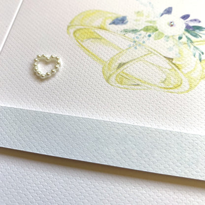 closeup of watercolour wedding rings card showing textured detail, raised sentiment strip,pearl and gem